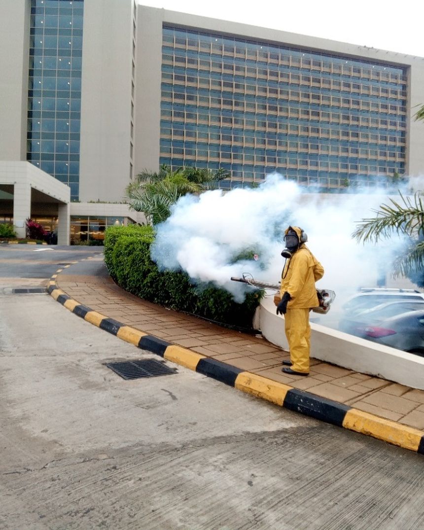 Technicien PULVA en tenue de protection réalisant une thermonébulisation devant un bâtiment à Conakry